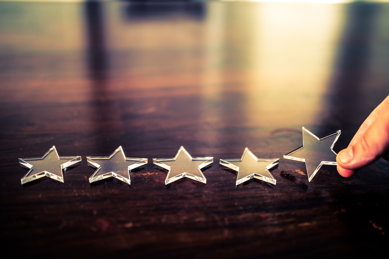 The best rating. Businessman arranging five transparent stars in row on a wooden desk. The office window is reflected on the desk